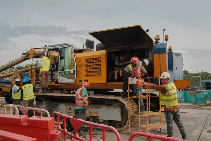 Construction crew in hard hats and hi-vis vests working around a tracked drilling rig